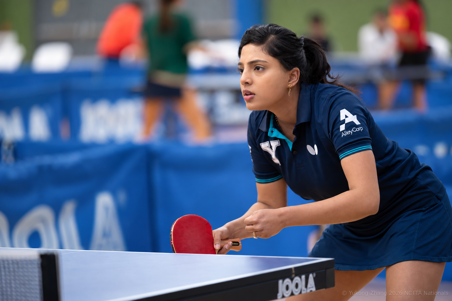 Yale Club Table Tennis player preparing to serve, with the AlleyCorp logo visible on her jersey sleeve.